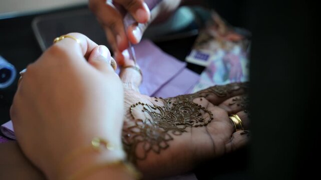 Woman dressed in traditional Indian clothes painting henna tattoo on woman palm. Hindu Traditions. Close up shot of the process