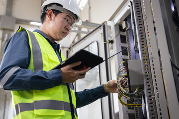 industrial maintenance, workplace safety, Male engineer in safety helmet and reflective vest inspecting electrical control panel with tablet and walkie-talkie, modern energy infrastructure