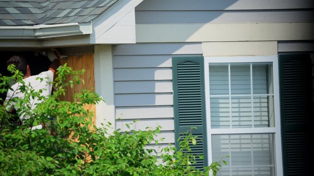 A worker removes old insulation and metal panels siding from the outside walls of the house
