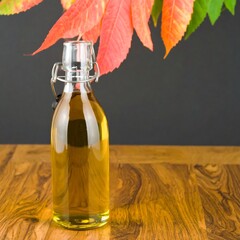 A glass bottle filled with a golden liquid sits on a wooden surface, with vibrant autumn leaves framing the top
