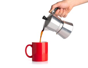 A hand pours freshly brewed coffee from a silver stovetop espresso maker into a red ceramic mug. The background is white