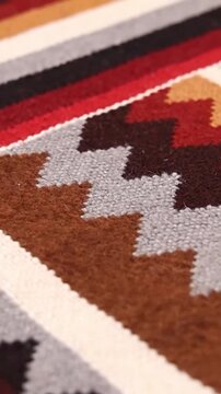 A closeup of a colorful woven rug with geometric patterns in red brown gray white and black