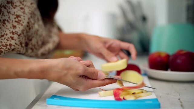 Adult hands peeling fresh apple on kitchen cutting board preparing healthy snack at home for daily nutrition