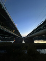 Fototapeta premium Warsaw, Poland - September 24, 2025: Two parallel bridges spanning a river at dusk, showcasing architectural design and urban infrastructure with reflections on water