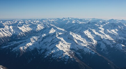 Aerial view of snow-capped mountain range under a clear blue sky, showcasing rugged peaks and valleys