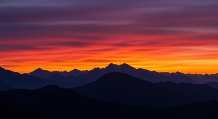 Fiery sunset over layered mountain silhouettes, vibrant orange and purple sky
