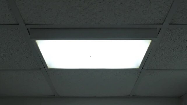 Dim office ceiling light flickering in dark room, ideal for suspenseful or mysterious atmosphere, creating unsettling feeling, horror background