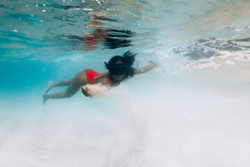 Woman in red swimsuit and mask glides underwater in tropical waters with sandy sea bottom
