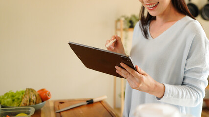 Woman organizing kitchen containers while using a tablet for meal planning on counter.