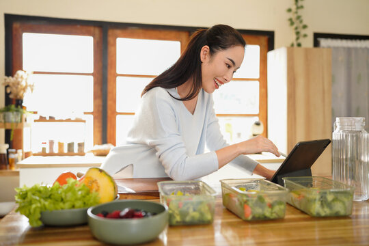 woman using digital tablet for recipe guidance while preparing healthy meals on kitchen counter.