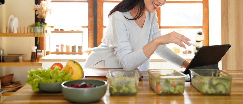 woman using digital tablet for recipe guidance while preparing healthy meals on kitchen counter.