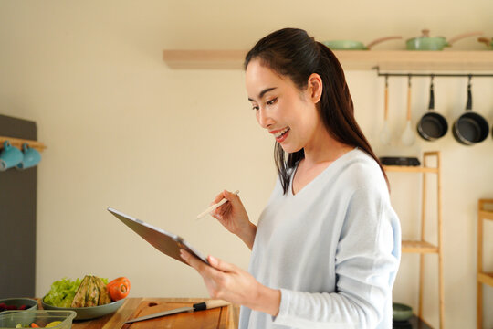 woman using digital tablet for recipe guidance while preparing healthy meals on kitchen counter.