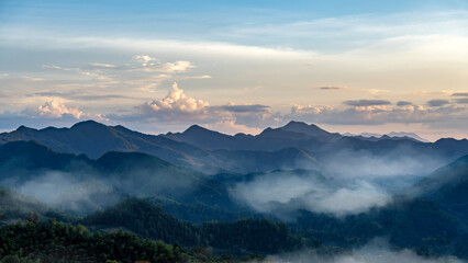 Misty mountain ranges under a clear sky with soft clouds