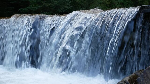 Swift mountain river with rapids and a mini-waterfall, forest in the background. Clear water cascades from a small height and sparkles in the sunlight. Concept of natural beauty, wilderness and pure