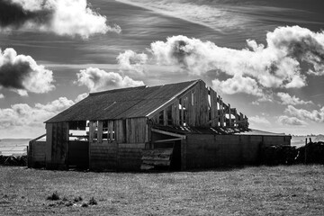 Partially collapsed barn in a rural field under a dramatic cloudy sky in black and white
