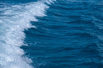 Dark blue and white ocean waves form diagonal lines on the sea surface, with fine white foam contrasting against the rippling water, demonstrating the power and movement of the ocean.