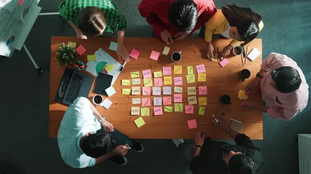 Top view of diverse business team putting hand together and clapping hand while brainstorming marketing idea or creative startup project by using sticky notes and stick at meeting table. Convocation.
