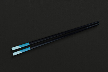Chopsticks in dark material, placed on a black textured background