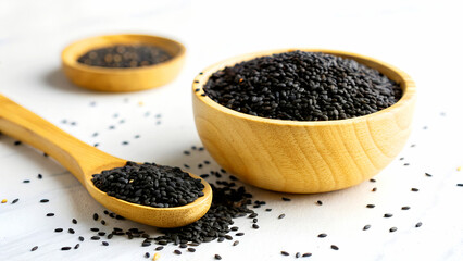 Black sesame seeds in a wooden bowl and spoon isolated on white background, offering a nutritious...