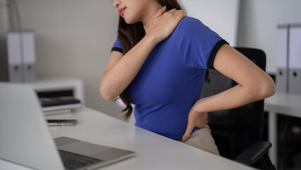 Asian woman office worker suffers shoulder back pain desk prolonged work focus workplace health ergonomics