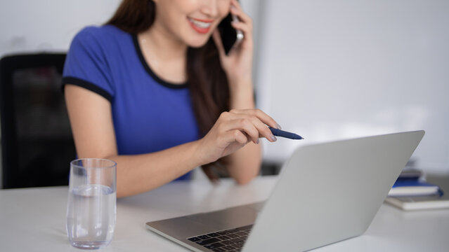 Adult Asian businesswoman remotely communicate laptop computer desk pen relaxed smile professional work office virtual meeting digital productivity