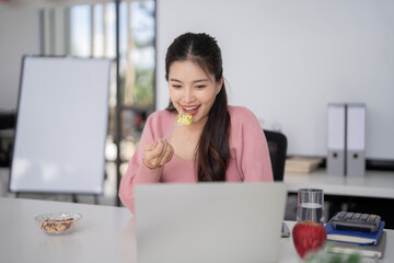 Asian adult businesswoman professional working laptop remote office enjoying snack break happy...