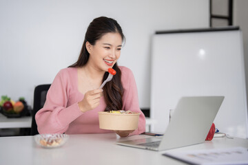 Asian adult female professional enjoys healthy lunch meal remote work environment laptop computer...