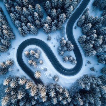 A winding road cutting through a snow-covered forest with evergreen trees lightly dusted in snow creating a serene winter landscape from an aerial perspective