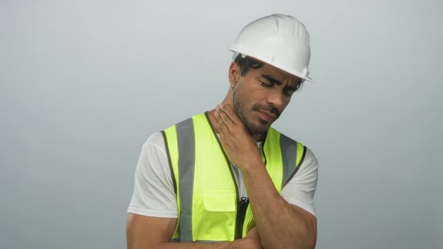 Hispanic man wearing hardhat helmet and neon safety vest coughing into fist in gray studio; discomfort.