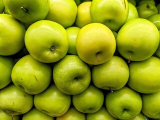 Close-up shot of a pile of bright green apples, showcasing their smooth skin and slight variations in color
