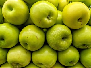 Close-up shot of a pile of bright green apples, showcasing their smooth skin and slight variations in color
