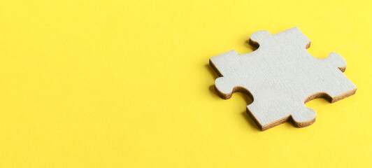 Single wooden jigsaw puzzle piece resting on a vibrant yellow background with ample copy space for...