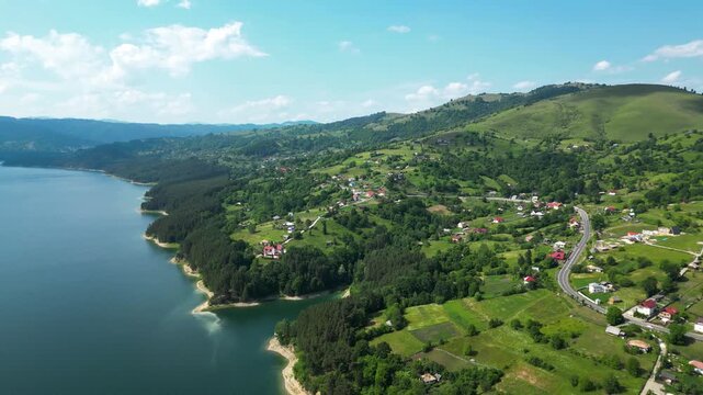 A breathtaking aerial view of Lake Bicaz surrounded by lush green hills and serene countryside, showcasing the natural beauty and peaceful landscapes of Romania. Drone panning right.