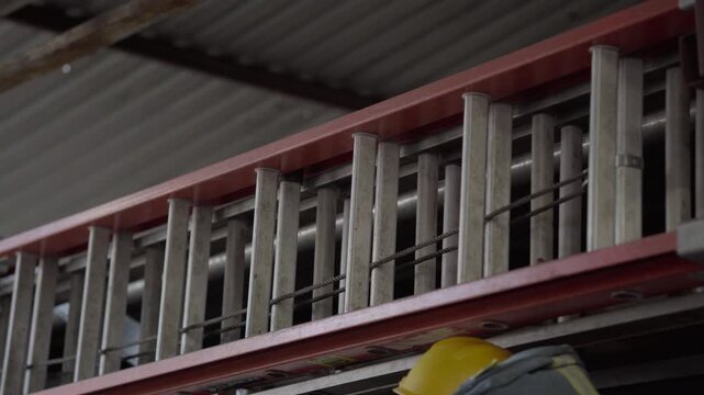 Aluminum ladder hanging inside an industrial hall, fixed under a metal beam with soft indoor light and factory atmosphere.