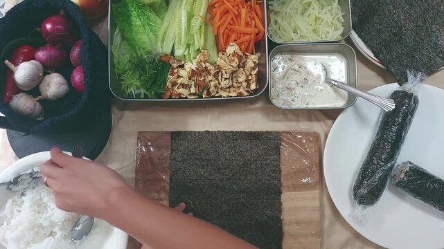Laying a sheet of seaweed and adding a layer of white steamed rice while surrounded by recipe ingredients for a kimbap or gimbap
