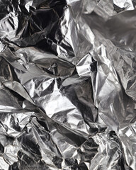 Crumpled aluminum foil reflecting light and shadow creating a dynamic metallic texture background. Material concept