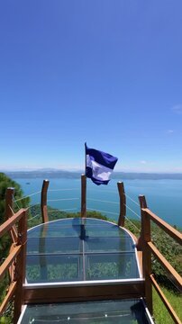 Flag of El Salvador flying with a view of Lake Ilopango in the background.