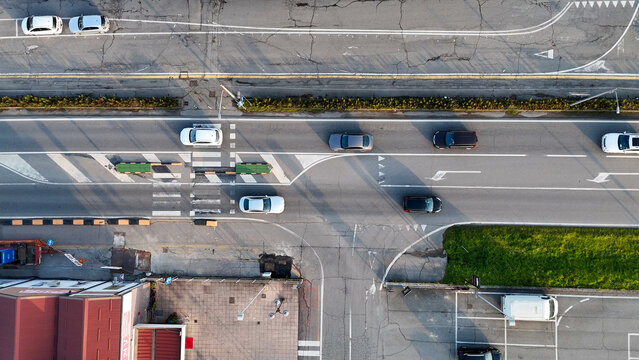 Castelvetro Piacentino aerial view showing traffic movement on a multi lane road with cars, crosswalks, an intersection, and commercial structures in an urban setting during daylight