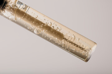 Clear brow gel tube on light background, minimalist macro beauty product shot.