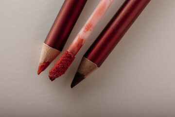 Two red lip pencils with red liquid lipstick on white background. Cosmetic color coordination concept.