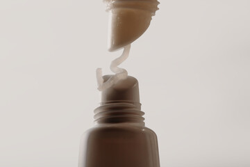 Two lip balms in macro view, one squeezing creamy texture onto the other. Clean light background.