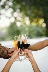Close-up of friends clinking glasses of beer and wine during an outdoor barbecue party, celebrating and enjoying good times together.