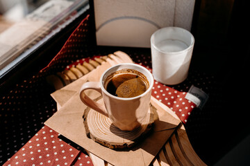 Small pink coffee cup with foam on window ledge in morning light, surrounded by candle and cozy details.