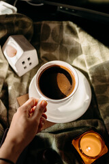 Woman holding white cup of coffee in cozy sunlight. Warm morning moment with comfort and calm.