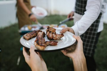 Close-up of grilled meat, potatoes, and vegetables cooking on a barbecue grill with smoke rising, showing delicious outdoor food preparation.
