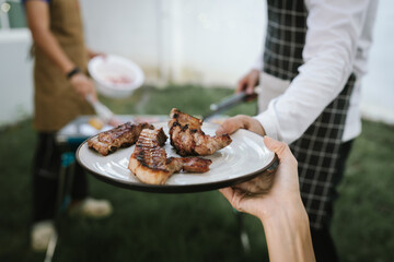 Close-up of grilled meat, potatoes, and vegetables cooking on a barbecue grill with smoke rising, showing delicious outdoor food preparation.