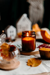 Cozy fall tea time with burning candle in dark glass and autumn leaves on wooden table.