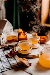 Steaming pumpkin tea in two transparent cups creates cozy autumn mood with candles and golden leaves.