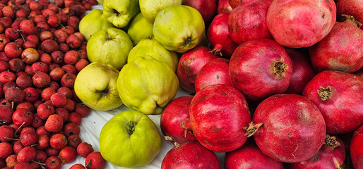 Colorful display of fresh fruits at a Spanish market: red hawthorn berries, green quinces, and ripe pomegranates. local produce, harvest