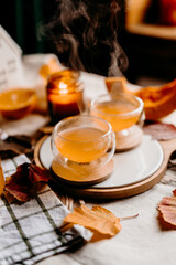 Cozy autumn table with two glass cups of steaming pumpkin tea and fall leaves. Warm peaceful home scene.